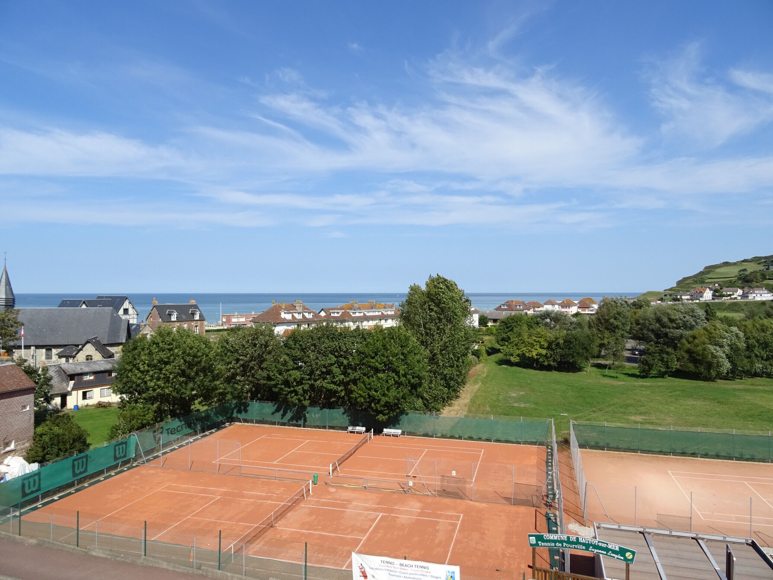 A tennis court with a view of a coastal town and a church steeple in the background.