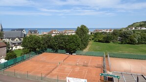 Un court de tennis offrant une vue sur une ville côtière et, au loin, sur le clocher d’une église.