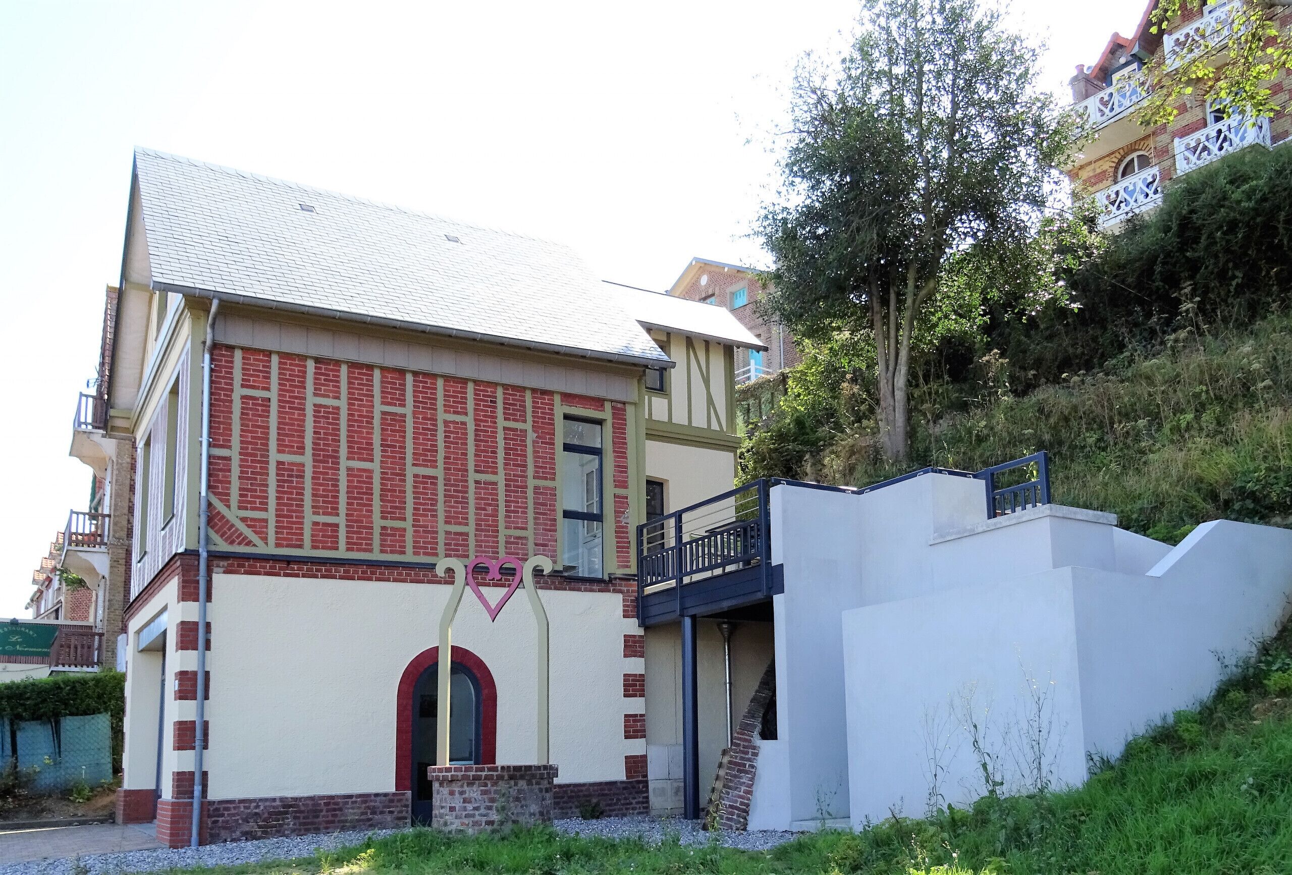 Un edificio de dos pisos con fachada de ladrillo rojo, sección superior blanca y un balcón con barandilla azul.