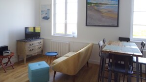 Un salon avec une télévision, un banc, une table à manger avec des chaises et un tableau accroché au mur.