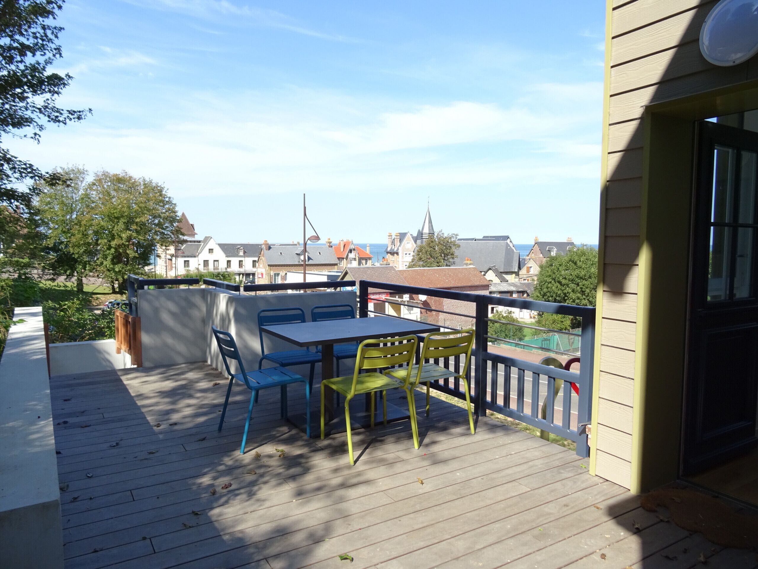 A wooden deck with a table and chairs, overlooking a town with buildings and a church spire.