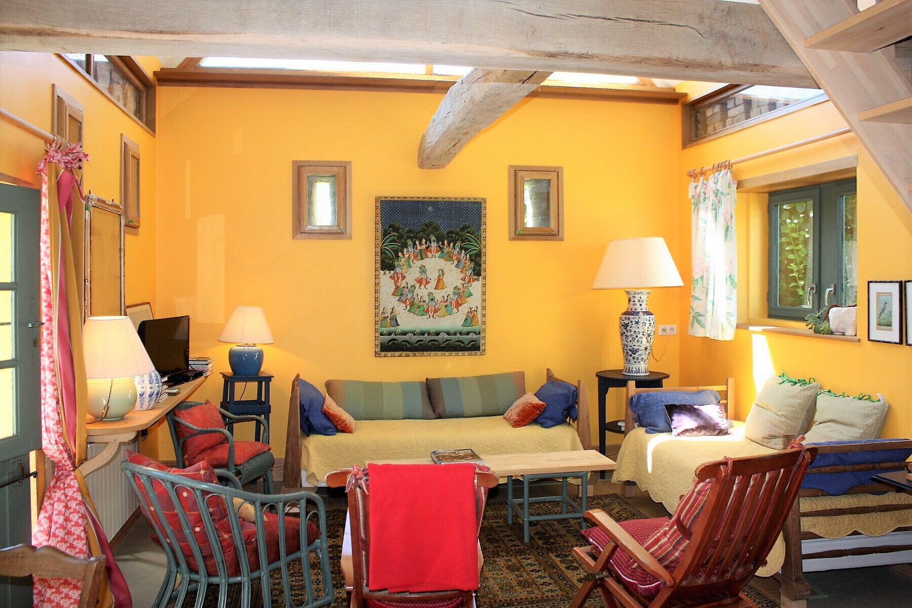 A cozy room with a yellow wall, a large painting, and a window with curtains.