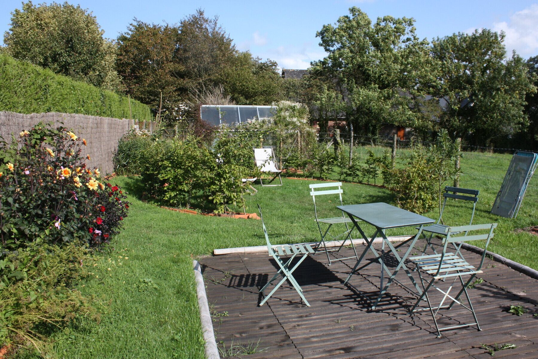 A garden patio with a table and chairs, surrounded by various plants and a brick wall.