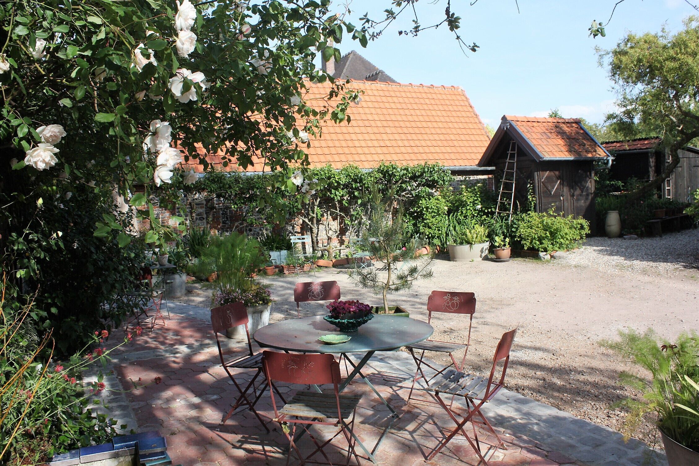 A patio with a round table and chairs, surrounded by potted plants and a garden.
