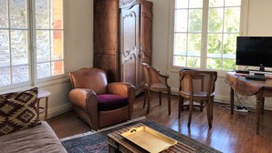 A living room with a leather armchair, a wooden cabinet, a television, and large windows. - Roses,turn of the century house 100 meters from the sea (Hautot-sur-Mer)