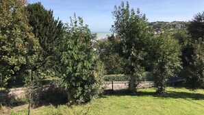A grassy area with trees and a distant view of a beach and buildings. - Roses,turn of the century house 100 meters from the sea (Hautot-sur-Mer)
