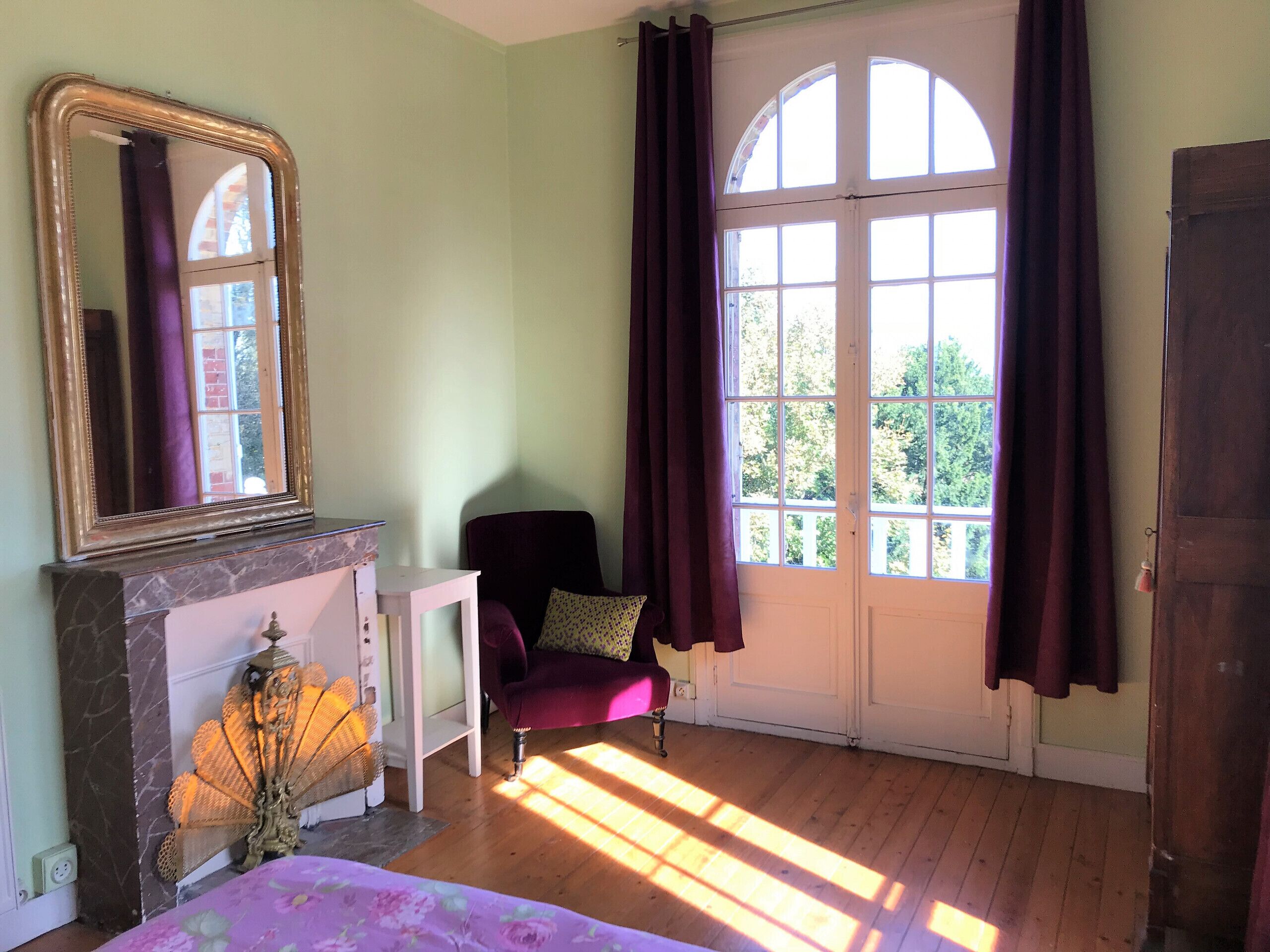 A room with a large arched window, a fireplace, a chair, and a bed.