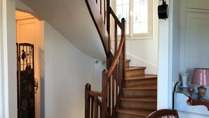 A wooden staircase with a handrail, a door with a decorative panel, and a window with a view of greenery. - Roses,turn of the century house 100 meters from the sea (Hautot-sur-Mer)