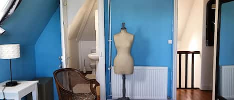 A room with blue walls, a wooden floor, a mannequin, a chair, and a table.