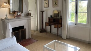 Une pièce avec une cheminée, un miroir, une lampe, un bureau et une fenêtre avec des rideaux.