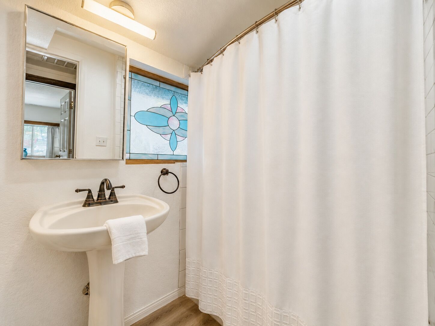 Un baño con un lavamanos blanco, un espejo, un tozaleta y una cortina de ducha.