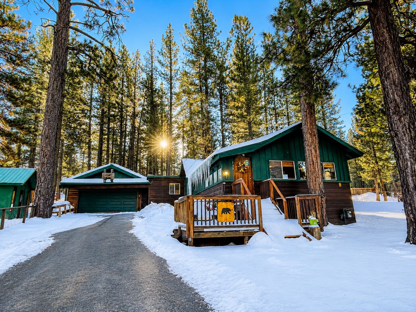 A cabin with a wooden deck and a snow-covered ground, surrounded by tall pine trees.