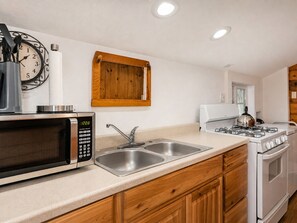 A kitchen with a microwave, sink, stove, and wooden cabinets.