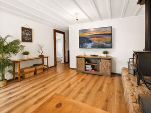 A living room with wooden flooring, a fireplace, a television mounted on the wall, a wooden cabinet, and a potted plant. - Evergreen Paradise - Hot Tub, Game Room, Pool Table, Foosball (Big Bear Lake)