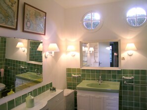 Une salle de bain avec deux lavabos, des carreaux verts et trois lampes fixées au mur.