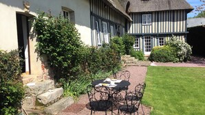 Ein traditionelles Fachwerkhäuschen mit einem Strohdach, einer Steintreppe und einem kleinen Garten mit Tisch und Stühlen.