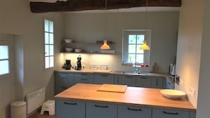 Eine Küche mit einer Holzausziehtafel, blauen Schränken, einer Kaffeemaschine und Pendelleuchten.