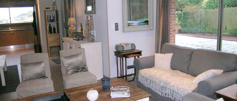 A modern living room with a grey sofa, a wooden coffee table, and a kitchen in the background.