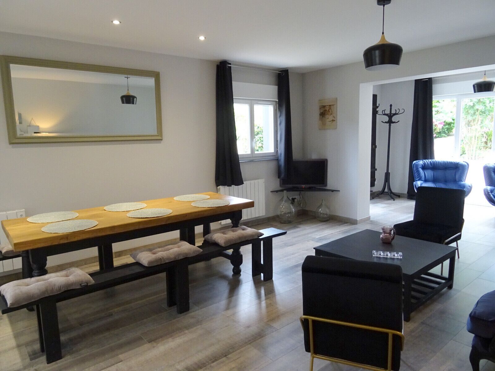 Uma sala de estar moderna com uma mesa de jantar de madeira, sofás pretos e uma televisão.