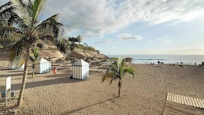 A beach with palm trees, a wooden deck, and a small hut. - Modern villa El Duque with pool (Costa Adeje)