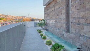 A balcony with a stone wall, a small garden with cacti, and a view of a parking lot and buildings in the background. - Modern villa El Duque with pool (Costa Adeje)