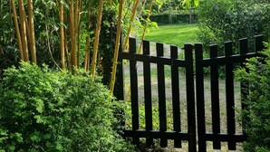 Una verja de madera da paso a un exuberante jardín con bambú y follaje denso.