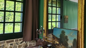 Una habitación con paredes verdes, una pared de piedra, un aparador de madera, un espejo grande y una ventana con cortinas.