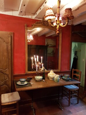 A dining area with a wooden table, chairs, a chandelier, and a large mirror with candles.