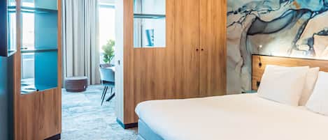 A hotel room with a large bed, wooden wardrobe, a desk with a chair, and a view of the outdoors.