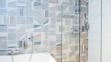 Une salle de bain moderne avec une douche à parois de verre, une baignoire blanche et un mur recouvert de carreaux aux motifs géométriques.