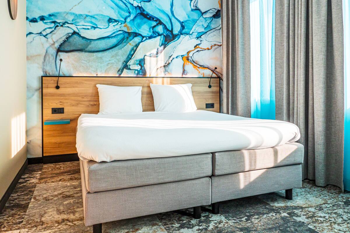 A modern bedroom with a large bed, wooden headboard, and a marble wall mural.