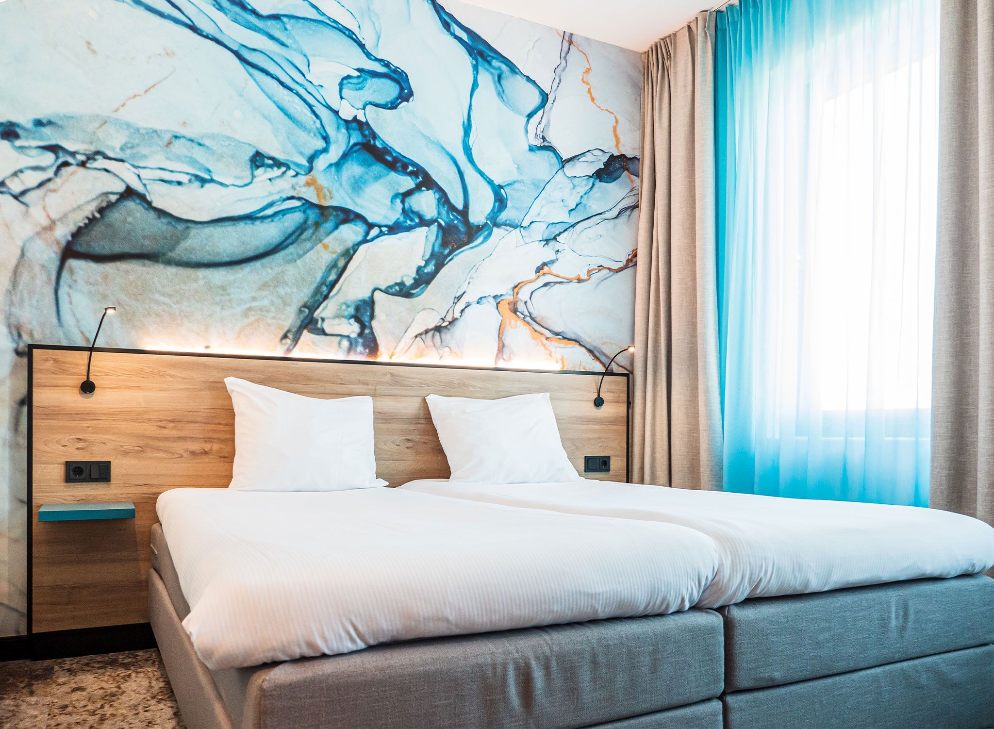 Habitación de hotel moderna con una cama grande, un cabecero de madera y un mural de mármol en la pared.