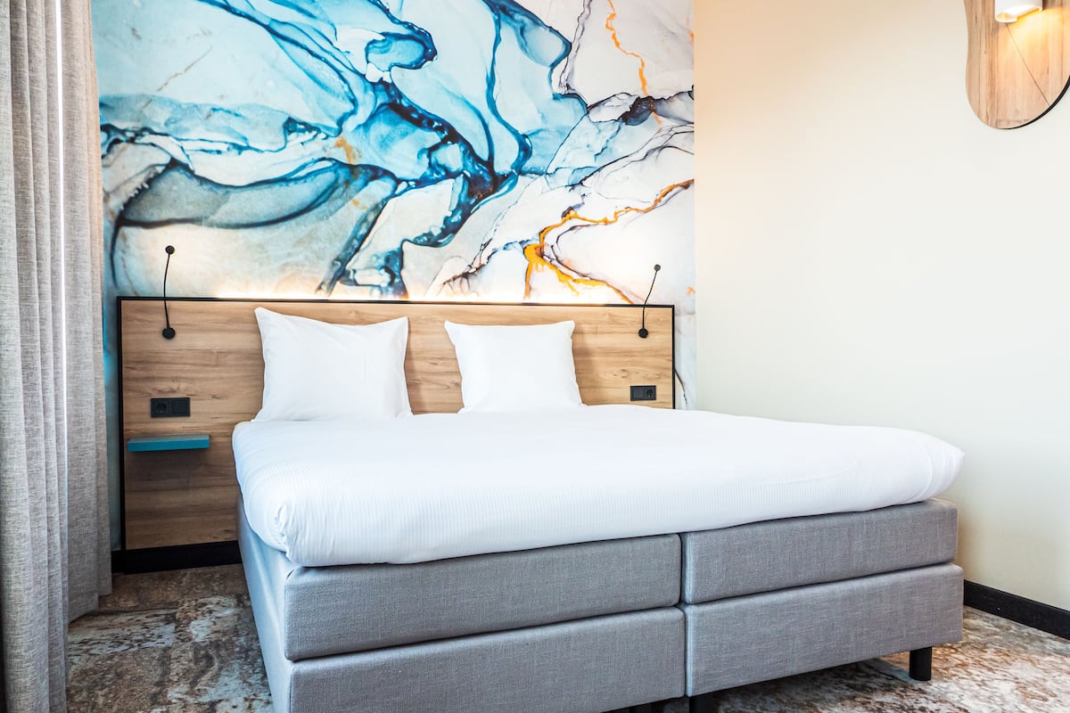 A modern bedroom with a large bed, grey upholstered headboard, and a marble-patterned floor.