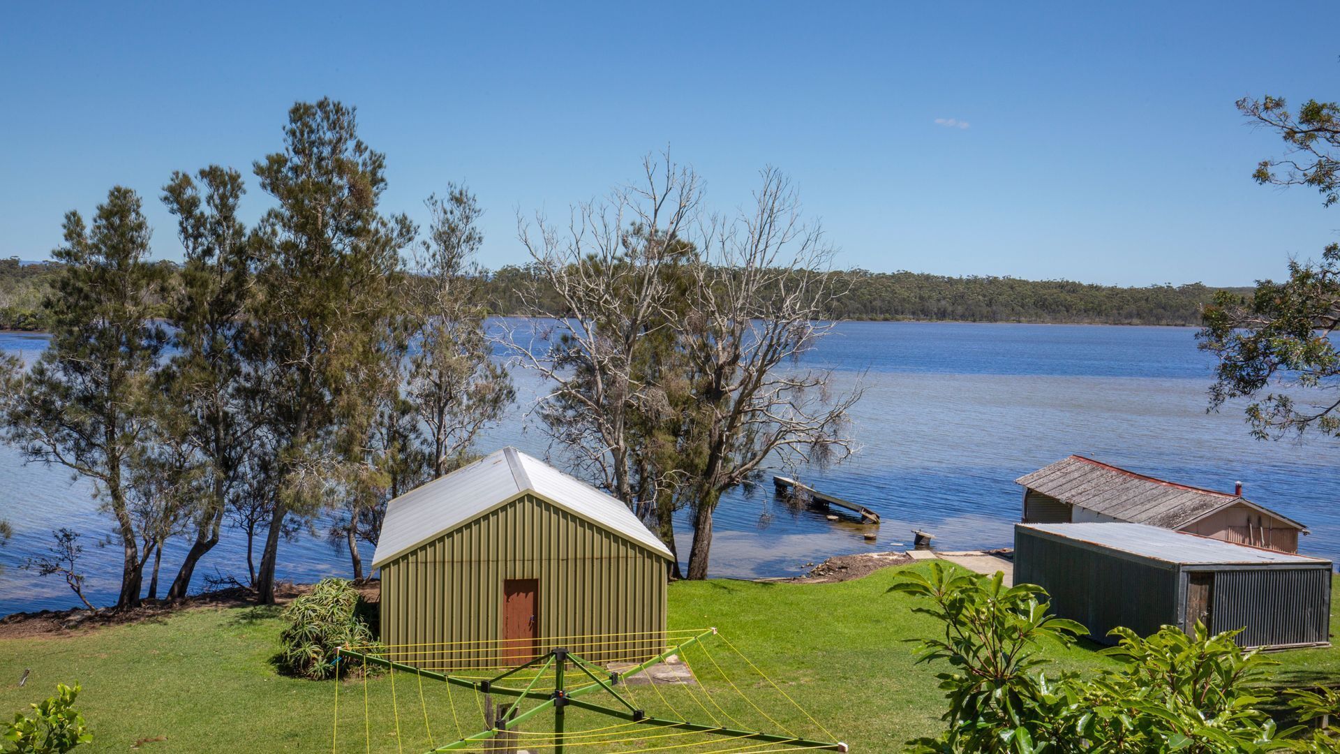 Une propriété au bord du lac comprenant un petit abri, un bâtiment plus grand doté d’un toit en pente et une zone herbeuse avec un fil à linge.