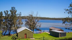 Une propriété au bord du lac comprenant un petit bâtiment, un abri de jardin et une jetée qui s’avance dans l’eau.