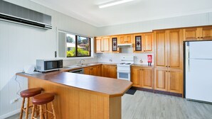 Une cuisine moderne avec des meubles en bois, un îlot central doté de tabourets, un four à micro-ondes, une cuisinière et un réfrigérateur.