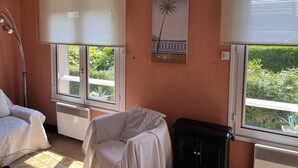 Una habitación con dos ventanas, un radiador, una silla, un armario negro y un cuadro colgado en la pared.