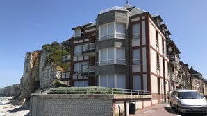 Un edificio costero con varios balcones, un muro de piedra y un paseo empedrado.