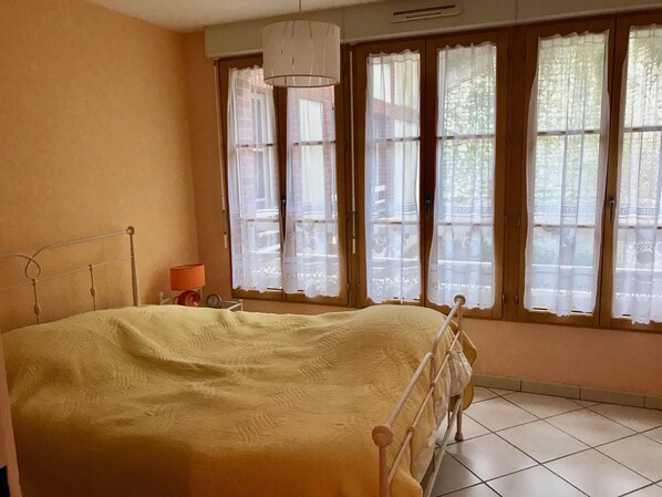 A bedroom with a bed, a nightstand, a lamp, and a window with curtains. - Pleine Mer (Yport)