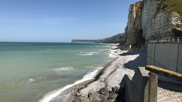 Vista costera con costa rocosa, un acantilado alto y un edificio distante en el horizonte.