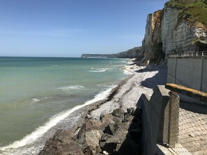 A coastal view with a rocky shoreline, a high cliff, and a distant building on the horizon.