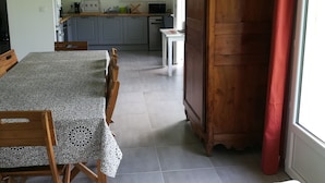 A dining area with a table and chairs, a wooden cabinet, and a view of a kitchen and garden through a window. - Le Cèdre (Varengeville-sur-Mer)