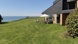 A modern house with a grassy lawn and a view of the sea.
