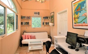 Um quarto aconchegante com uma cama, uma escrivaninha com um computador, uma estante de livros e uma janela com vista para o verde.