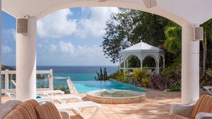 Un espace piscine avec des chaises longues, un jacuzzi et un belvédère offrant une vue sur l’océan.