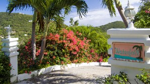 Un sentier mène à un panneau indiquant « Cascade », le tout étant entouré d’une végétation luxuriante et de plantes en fleurs.