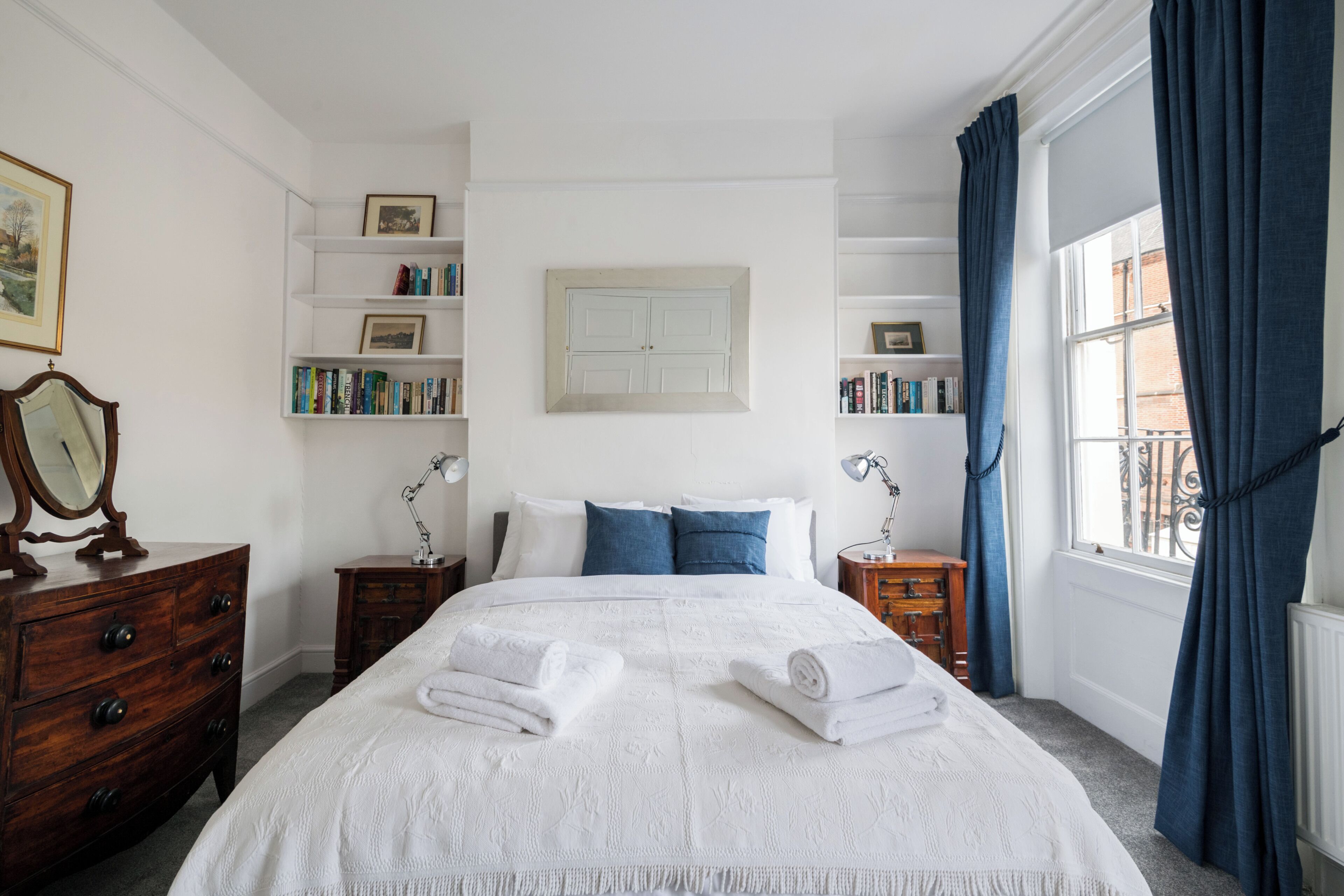 Ein ordentlich eingerichtetes Schlafzimmer mit einem großen Bett, Nachttischen, einem Schminktisch und einem Bücherregal.