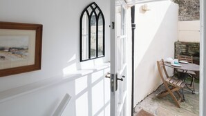 A white interior with a door leading to an outdoor area. There is a framed picture on the wall, a window with a black frame, and a table with chairs outside.