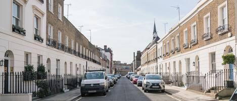 Una calle bordeada por edificios de dos pisos, coches estacionados y un cielo despejado.