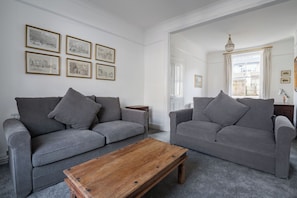 A living room with two grey sofas, a wooden coffee table, and framed black-and-white artwork on the walls. - At Home in Chelsea (London)